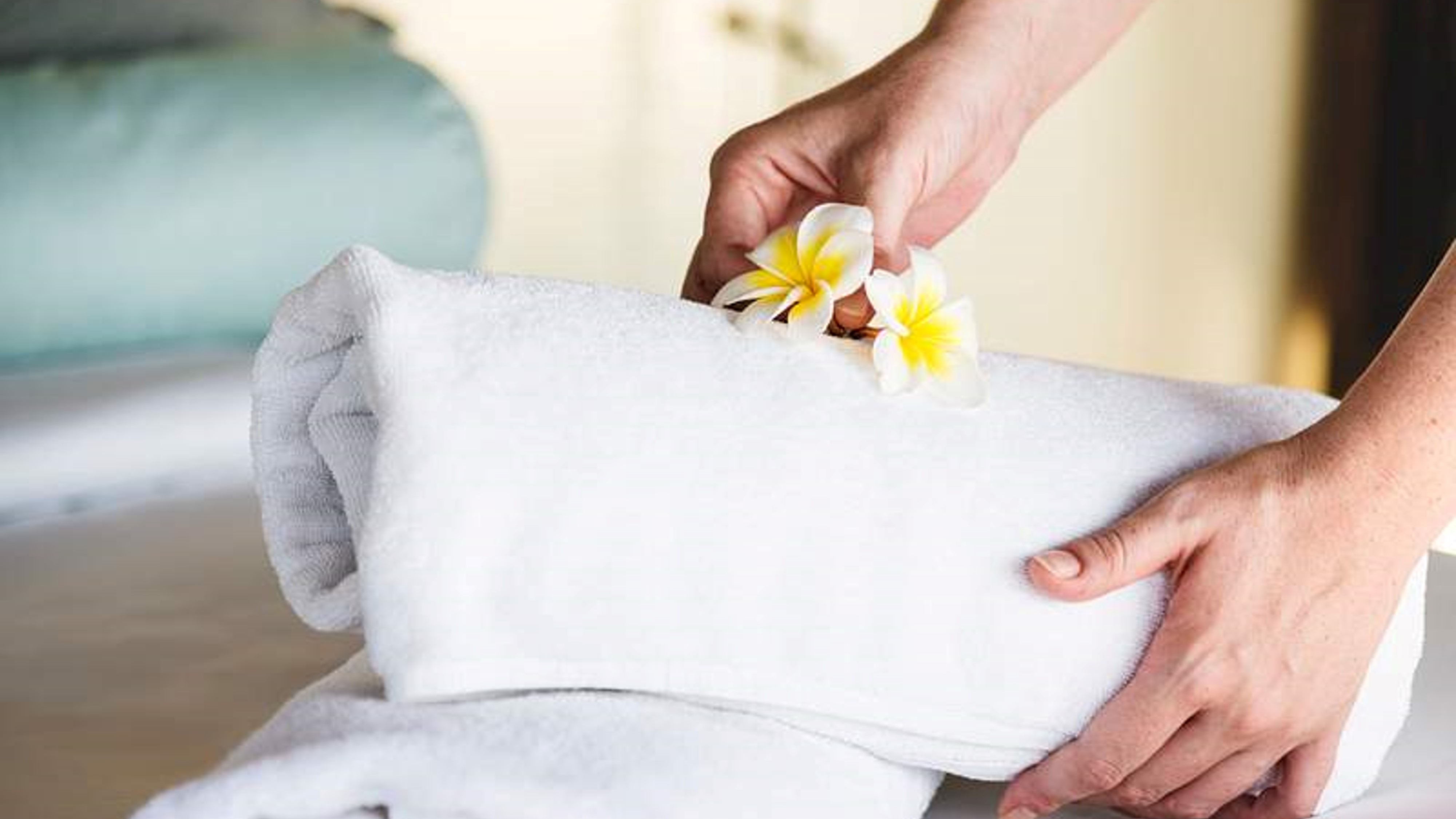 Hotel employee placing flowers on top of freshly changed sheets after preparing the room for a new guest